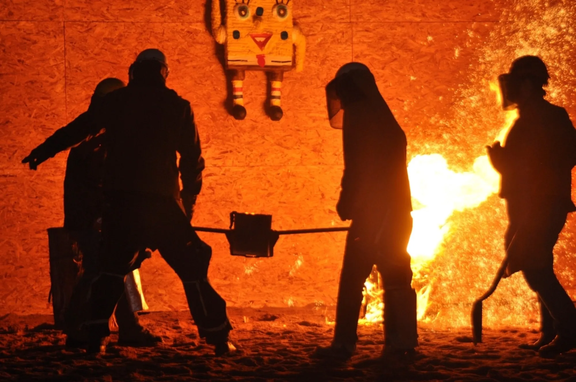 Workers in protective gear beside a glowing industrial furnace